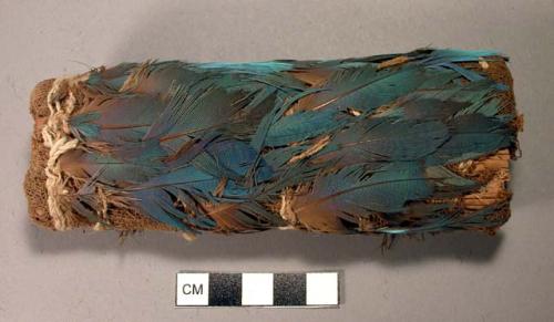 Organic, feathered object, cylinderical, covered with brown cloth and feathers