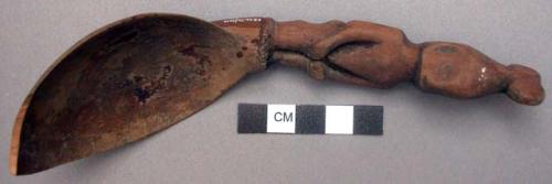 Wooden spoon, handle carved in human effigy: hands resting on flexed knees, hair