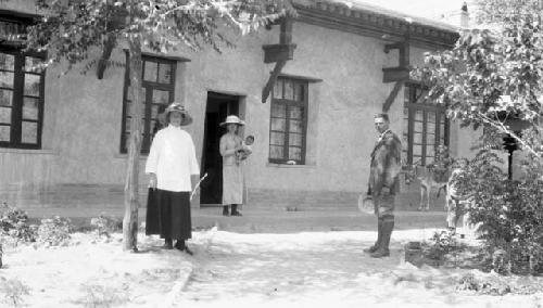 Man and two women, one holding baby outside of building