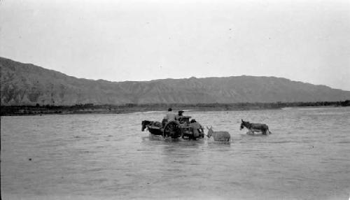 People crossing river with horse-drawn cart and two donkeys