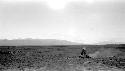 Person sitting in desert, mountains in distance