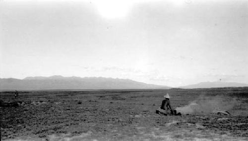 Person sitting in desert, mountains in distance