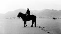 Woman sitting on pony in desert by mountains