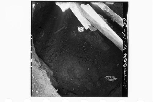 Funeral objects in place in Burial 1a.  Top of pottery vase, whistle, and carved
