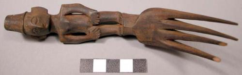 Wooden fork, 4 prongs, handle carved in human effigy: hands resting on flexed kn