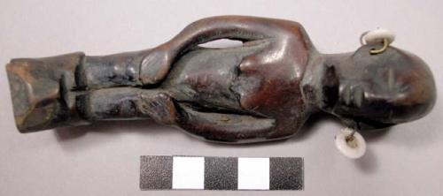 Wooden figurine, carved in human effigy: female(?), hands resting on flexed knee