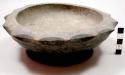 Carved wooden bowl with scalloped edges, base rim pierced by two holes for hangi