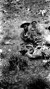 Men sitting at campfire holding bowls, rocky hillside