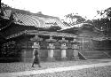 Person walking in front of Japanese building, stone lanterns