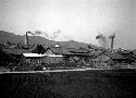 Smoke rising from building smokestacks, hills in background