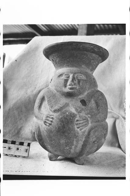 Tetrapodal human female effigy, spouted lost color pottery jar.