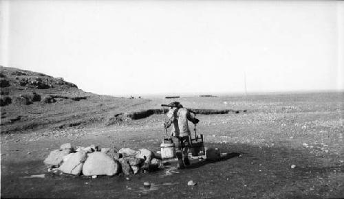 Person with buckets on shoulder carrier in desert