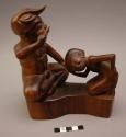 Carved wooden figure - Goesti - puffing a cheroot and scolding his wife