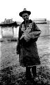 Older man wearing hat and chuba, building in background