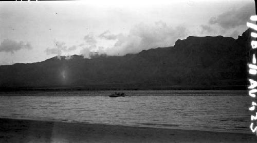 Boats on distant shore of river, mountainour background