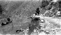 One person walking, one riding on rocky trail along river