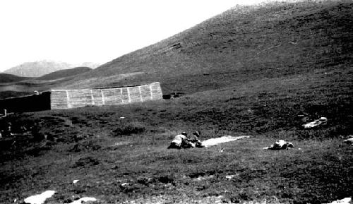 Men laying out cloth(?) on field, walled structure at left