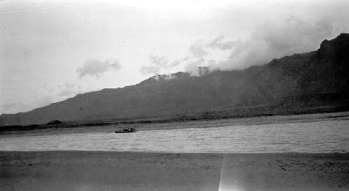 Boats on distant shore of river, mountainour background