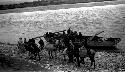 Boat moored at river edge, people and horses on shore