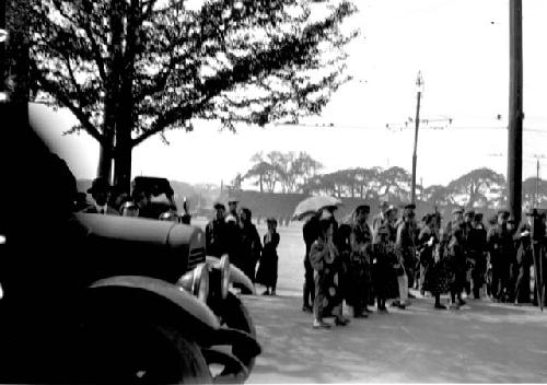 Car and group of people on road, one holding umbrella