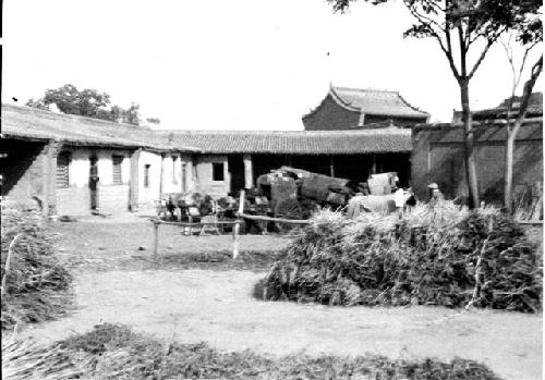 Carts gathered in yard with houses, hay(?) leaning on racks