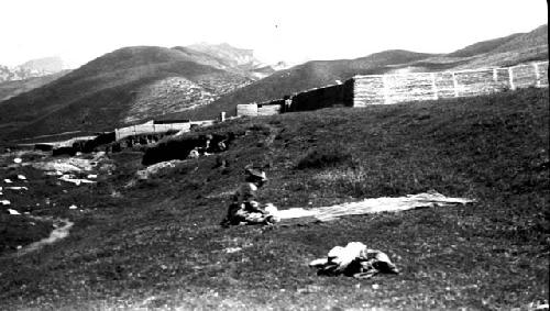 Person laying cloth in field, walled structure behind