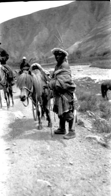Tibetan men and horses, one with rifle, river background