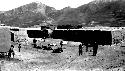 People and animals in yard with low building, background mountains