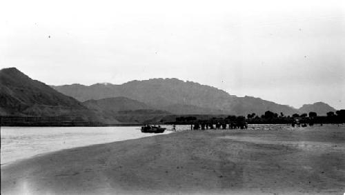 One boat on river, people on shore, mountain background