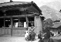 Man and children on platform outside building, mountain background