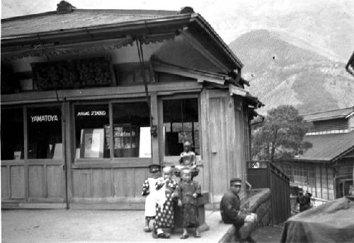 Man and children on platform outside building, mountain background