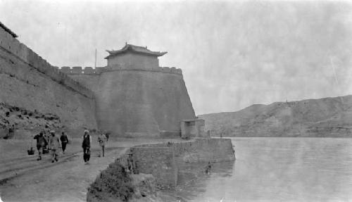 People walking near wall enclosing building on river