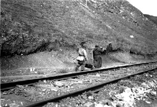 Men carrying heavy object along railriad tracks
