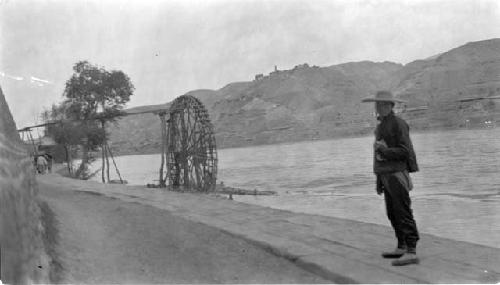 Man standing near waterwheel in river