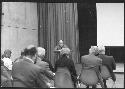 Gordon Willey seated at a desk, speaking to an audience