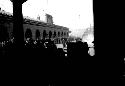 People gatheres outside arched building (railroad station?)