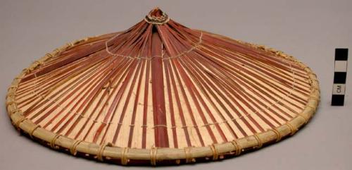Hat, shallow cone of natural wood with red cane strips radiating from the top ce