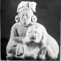 Ceramic figurine, seated human with arms around crouching feline