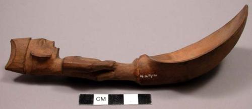 Wooden spoon, handle carved in human effigy: hands resting on flexed knees, sadd