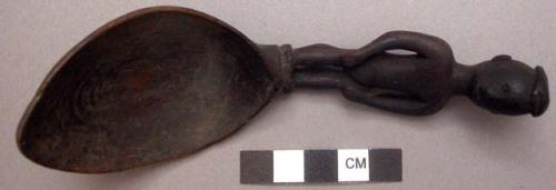 Wooden spoon, handle carved in human effigy: hands resting on flexed knees, flat