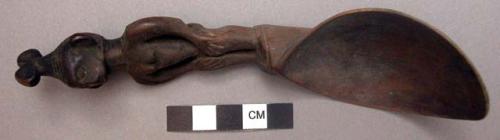 Wooden spoon, handle carved in human effigy: hands resting on flexed knees, hair