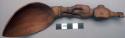 Wooden spoon, handle carved in human effigy: hands resting on flexed knees, male