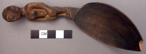 Wooden spoon, handle carved in human effigy: hands resting on flexed knees, fema