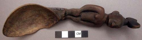 Wooden spoon, handle carved in human effigy: hands resting on flexed knees, hair