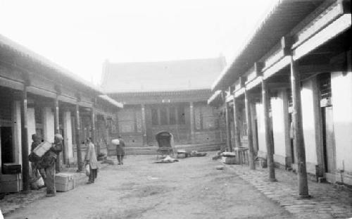 People standing outside buildings, cart in road