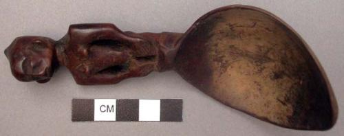 Wooden spoon, handle carved in human effigy: hands resting on flexed knees, fema