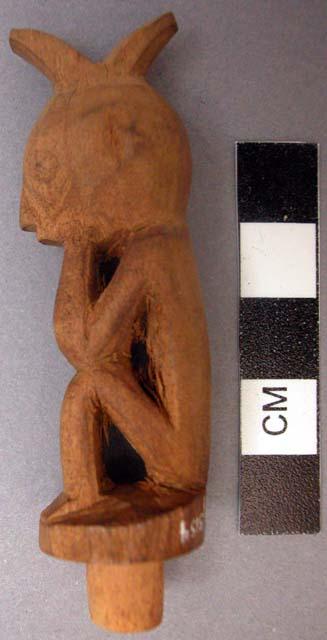 Carved wooden bottle stopper figure of man with hands on face, elbows on knees.