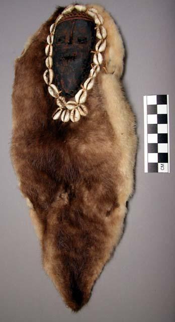 Small wooden mask surrounded by a frame of cowrie shells,mounted on fur pelt