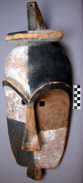 Mask, carved wood, anthropomorphic face, arched brows, disc top, pigmented