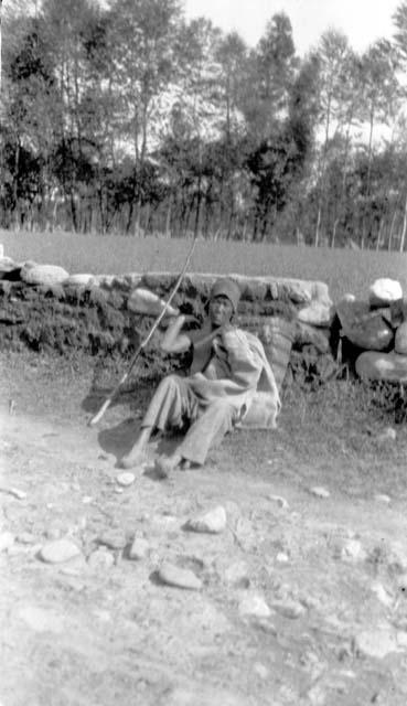 Person resting against stone wall along road